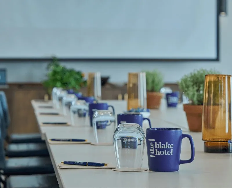 Corporate meeting room with table and the blake hotel cups and pens
